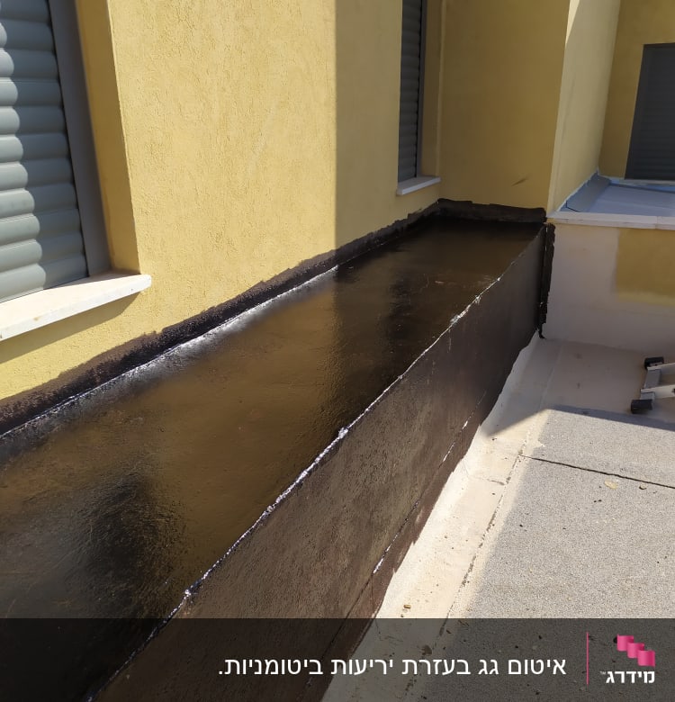 משטח אטום בזפת שחורה ליד קיר חיצוני